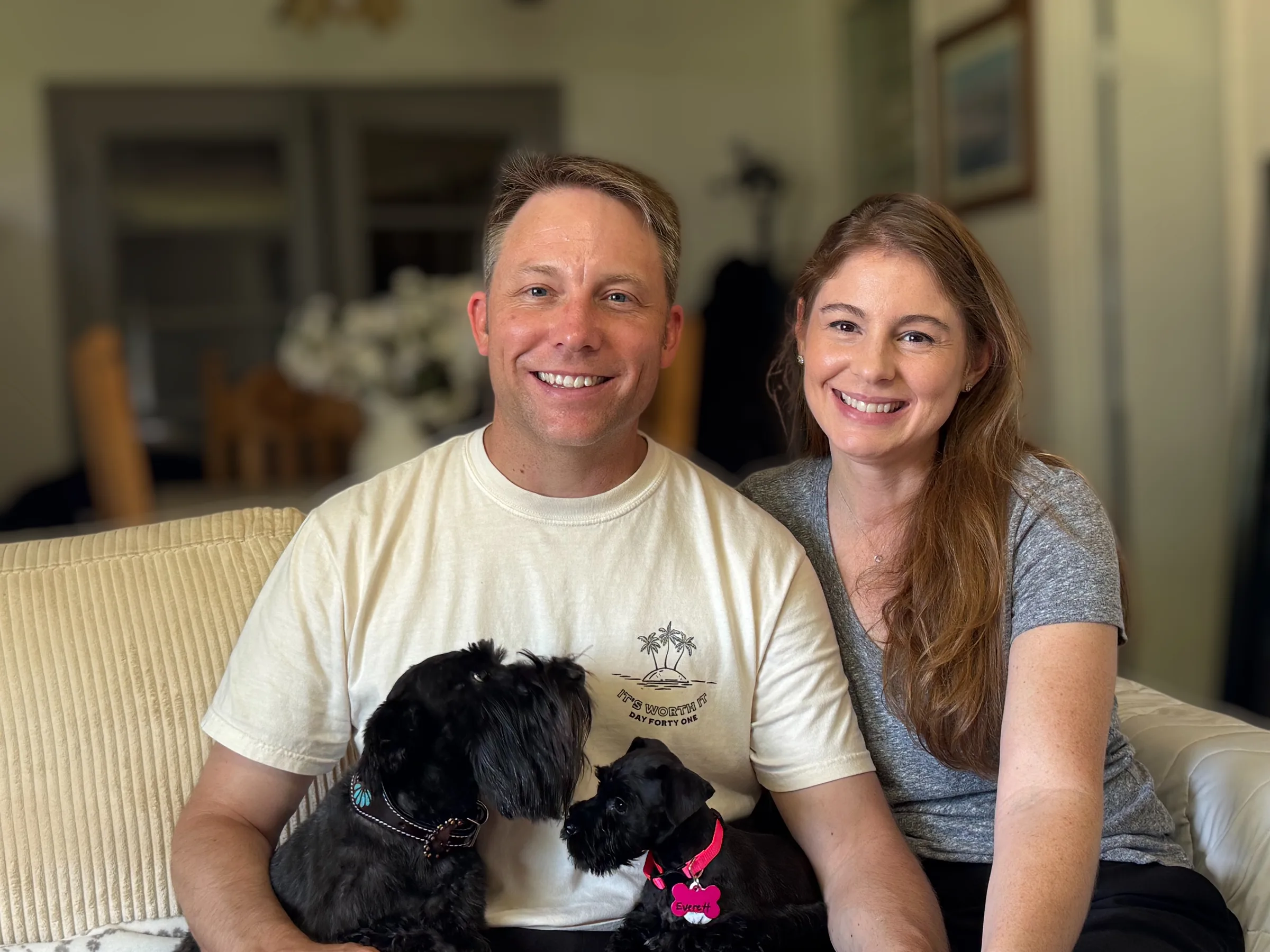 A couple on the couch with their two black miniature schnauzers